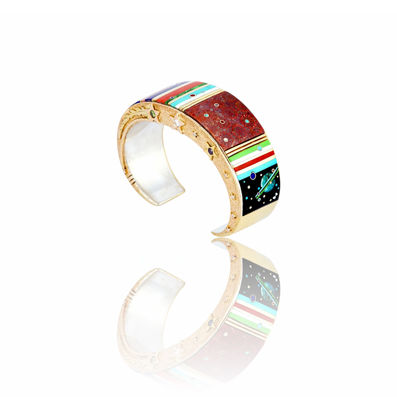 14k gold and sterling silver bracelet by Jesse Monongya featuring fine micro-inlay of turquoise, jet, lapis, coral, sugilite, mother-of-pearl, and fossilized coral arranged in a celestial space motif with planets and stars, accented by gold fine-line spacers, textured gold sides with diamond shooting-star details, signed “JMonongya.”