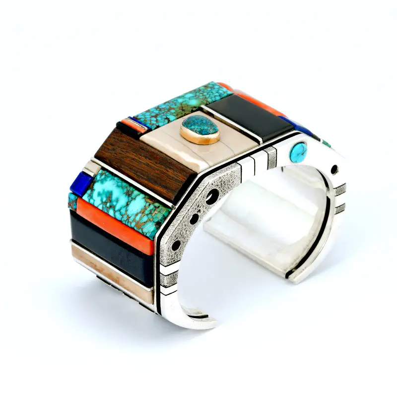Navajo jeweler Wes Willie created a sterling silver inlay bracelet featuring turquoise, coral, lapis, ironwood, fossilized ivory, jet, and fine-line silver bars. The bracelet includes a Lone Mountain turquoise stone set in gold and a hallmark inside.