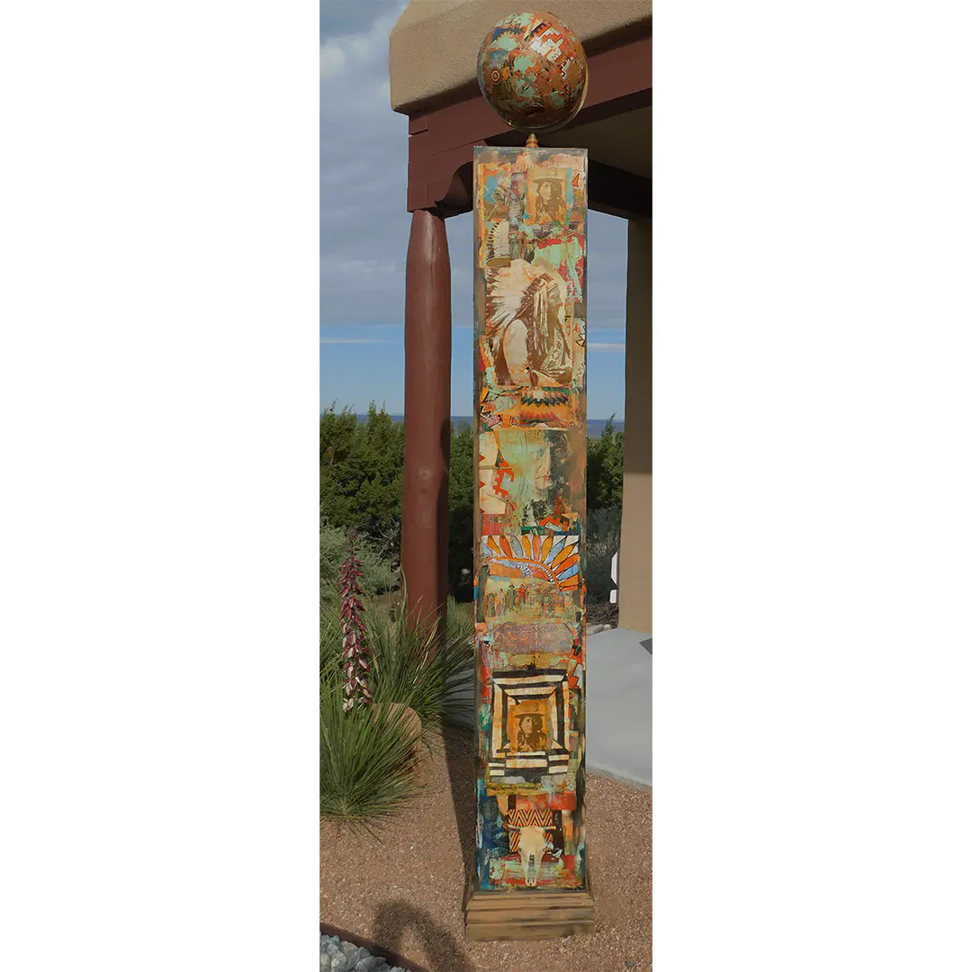 101x14 Native Totem by Dave Newman is a tall mixed-media totem sculpture featuring layered imagery, geometric patterns, and earthy Southwestern colors. The vertical piece includes vintage-style portraits, symbolic motifs, and textured collage elements in turquoise, rust, gold, cream, and black, topped with a decorated sphere. Installed outdoors near desert landscaping and adobe-style architecture, the work has a ceremonial, architectural presence.