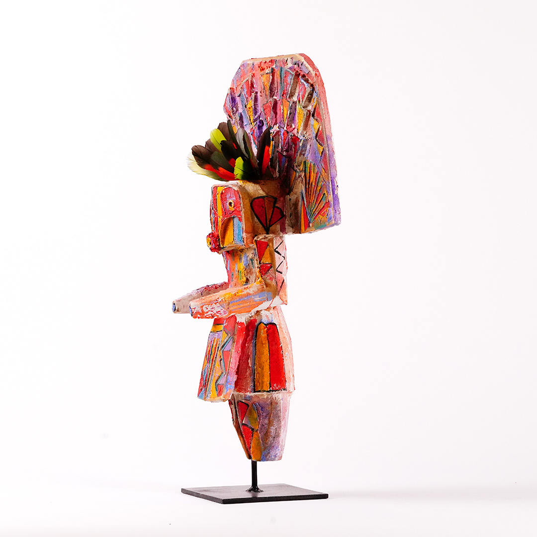 Side view of a stylized Navajo Yei wood sculpture by Sheldon Harvey, hand-painted in vivid colors with feather accents and mounted on a black metal base.