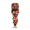 Colorful carved wooden figure on a stand, decorated with bold geometric patterns, zigzags, triangular motifs, and feather-like elements, with a stylized human face and body in bright red, orange, blue, purple, and black against a white background.