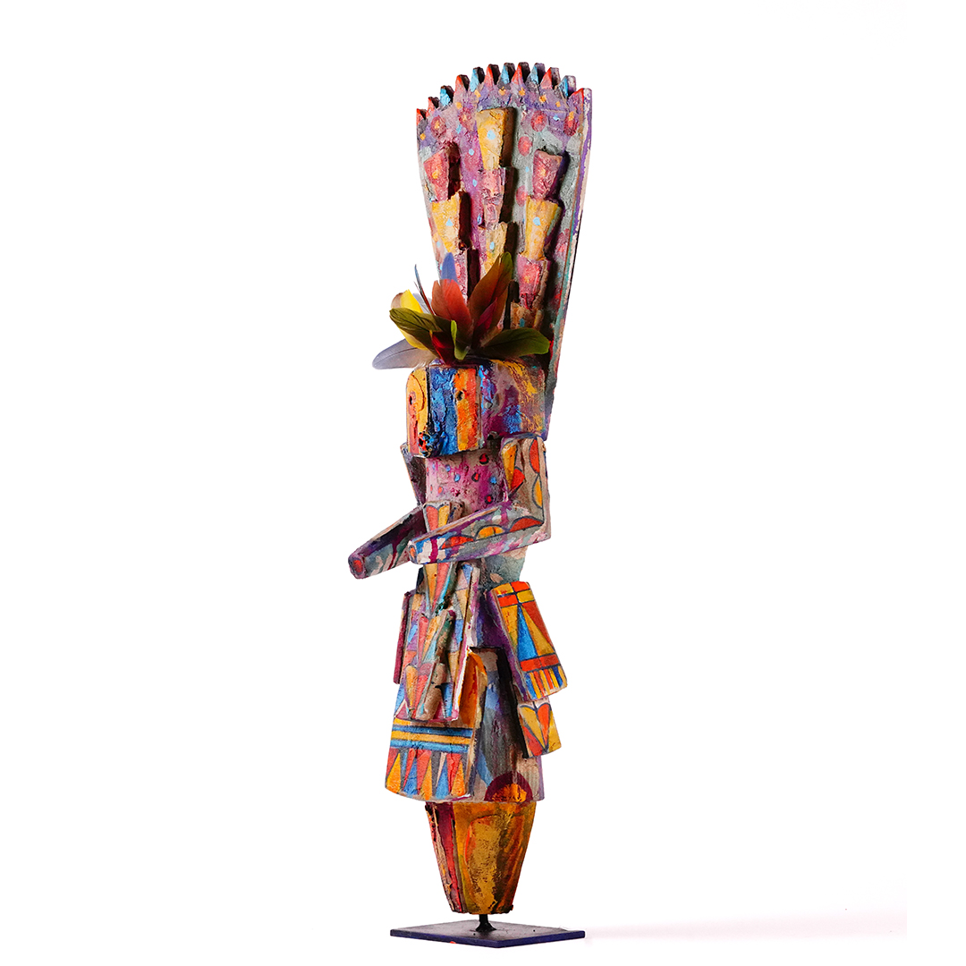 Side view of a brightly painted stylized Navajo Yei wood sculpture by Sheldon Harvey with geometric patterns, a tall headdress, and multicolored parrot feathers, mounted on a metal stand.